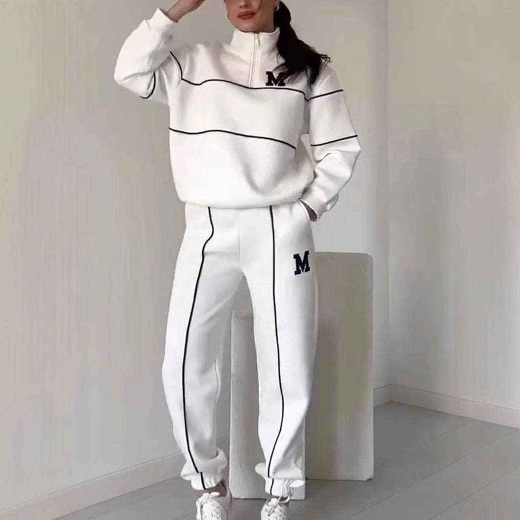Female model wearing white hoodless pullover sweatshirt and matching sweatpants with black stripe details and "M" lettering, styled for comfort and casual wear